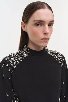 Black mini dress with crystal and rhinestone embellishments concentrated on shoulders and sleeves, high neckline.