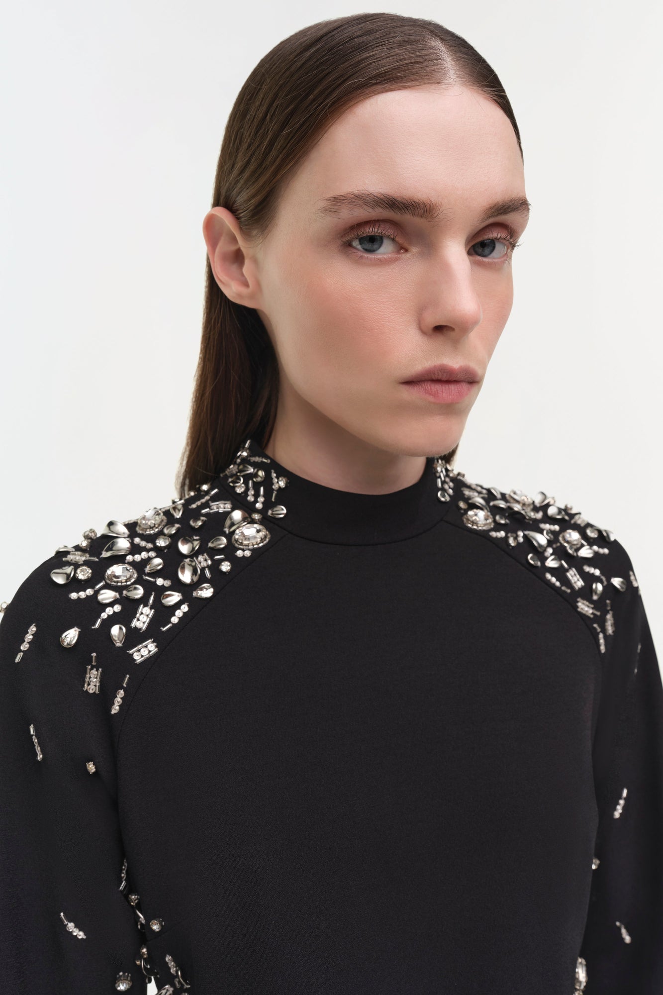 Black mini dress with crystal and rhinestone embellishments concentrated on shoulders and sleeves, high neckline.