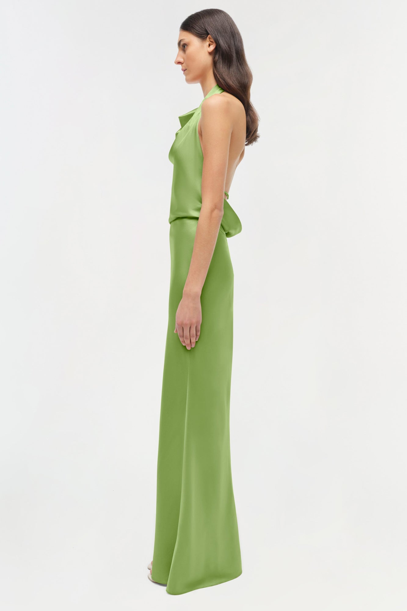 Woman wearing a green satin halter gown with draped detail at the waist, shown in side profile.
