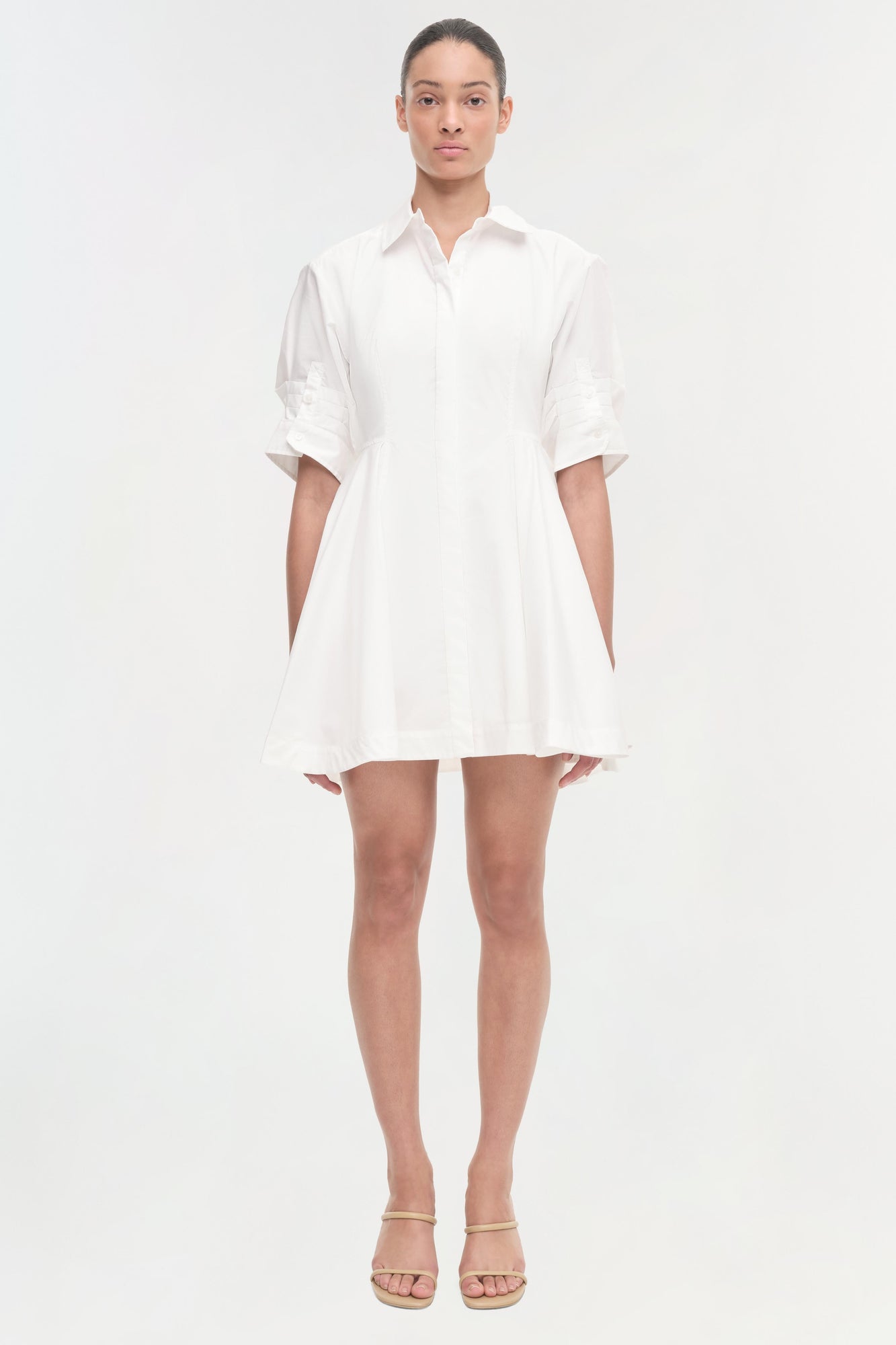 Woman wearing a white button-up shirt dress with rolled sleeves and a flared skirt, paired with beige sandals.