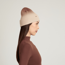 Side view of woman wearing a beige knit ombre beanie against a light gray background