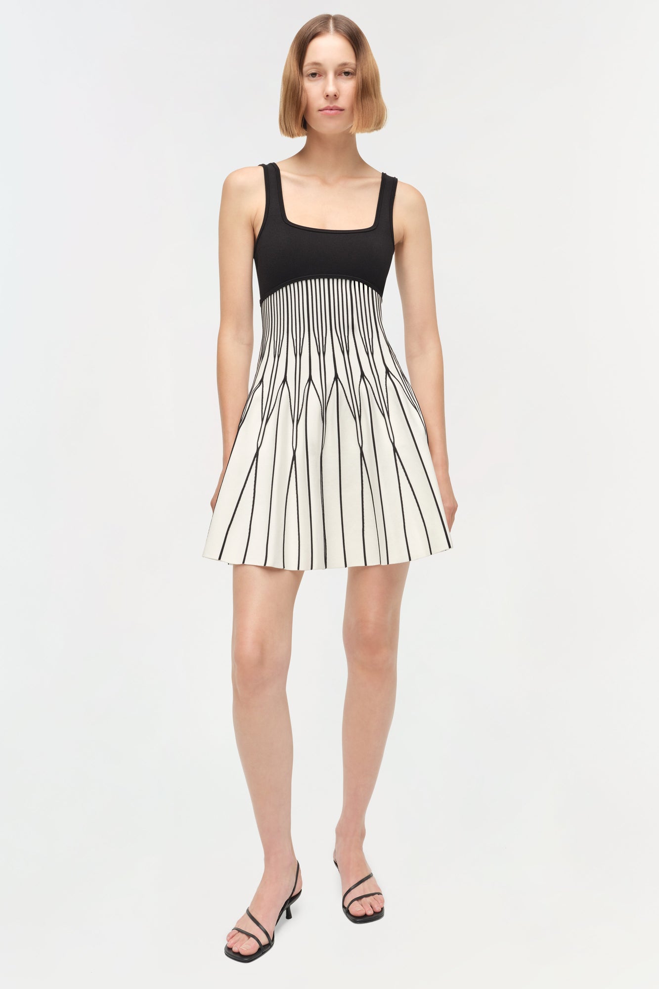 Black and white knit mini dress with square neckline and pleated skirt worn with black strappy sandals.