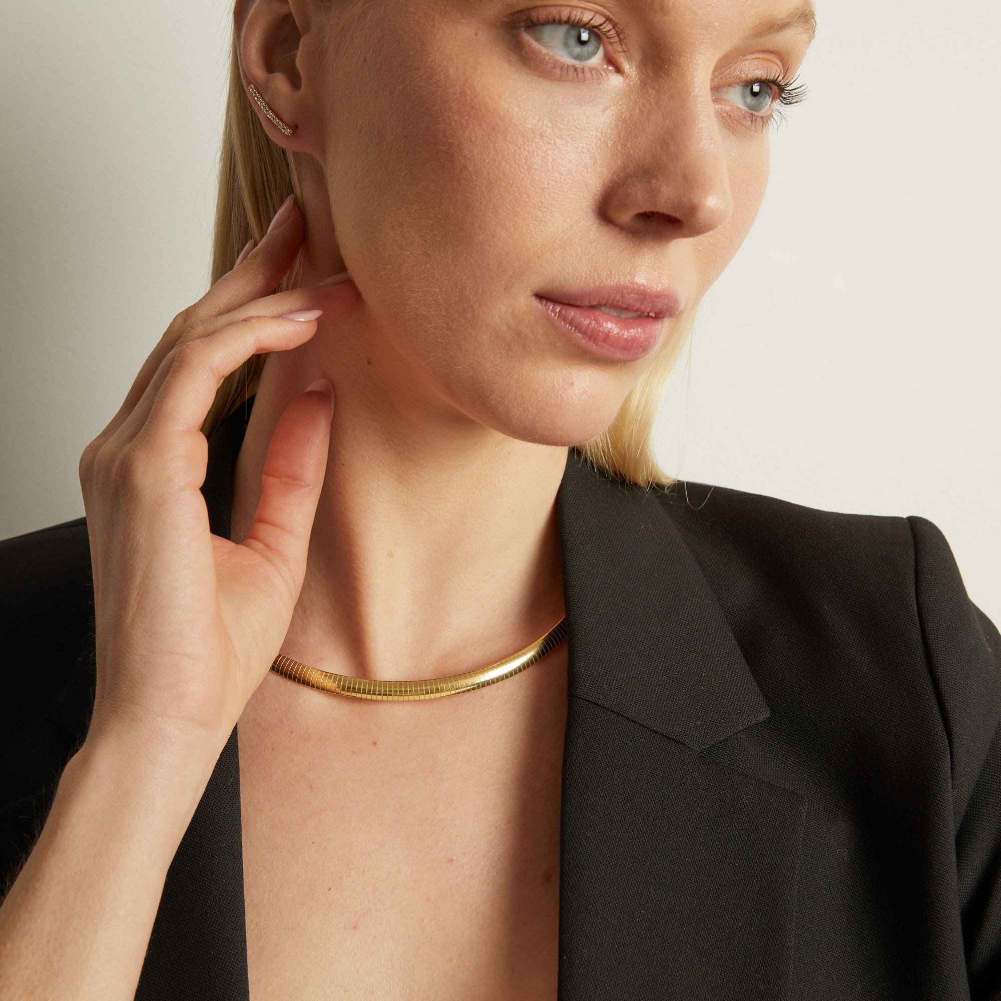 Model. Woman wearing a gold necklace with a neutral background