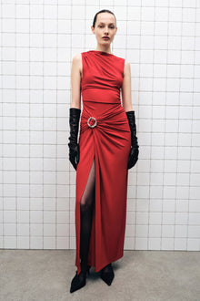 Woman wearing a sleeveless red jersey gown with ruched waist detail and high slit, paired with black gloves.