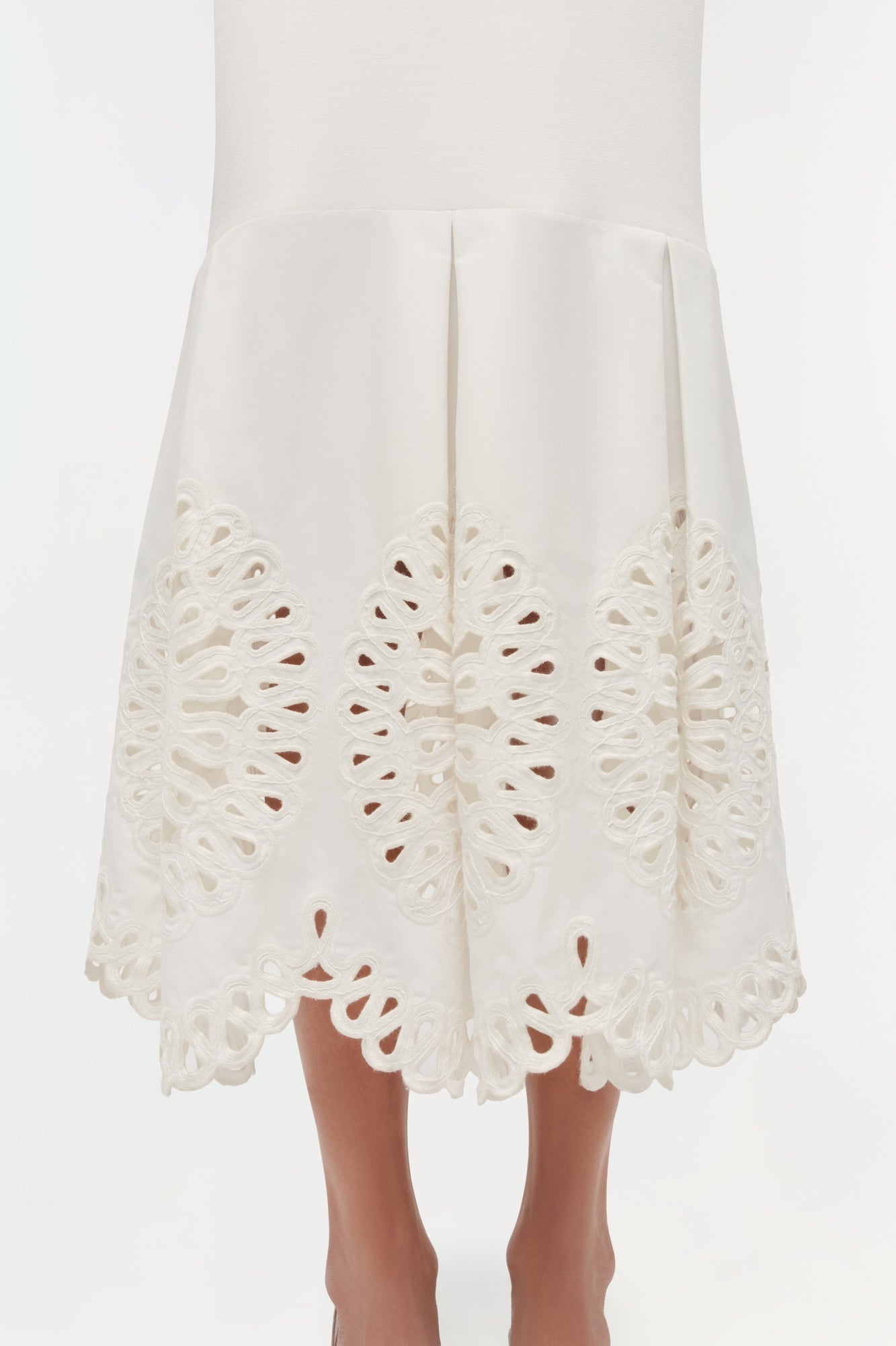 Cream knit midi skirt with ornate cutout embroidery detail along the hem, displayed on a model.