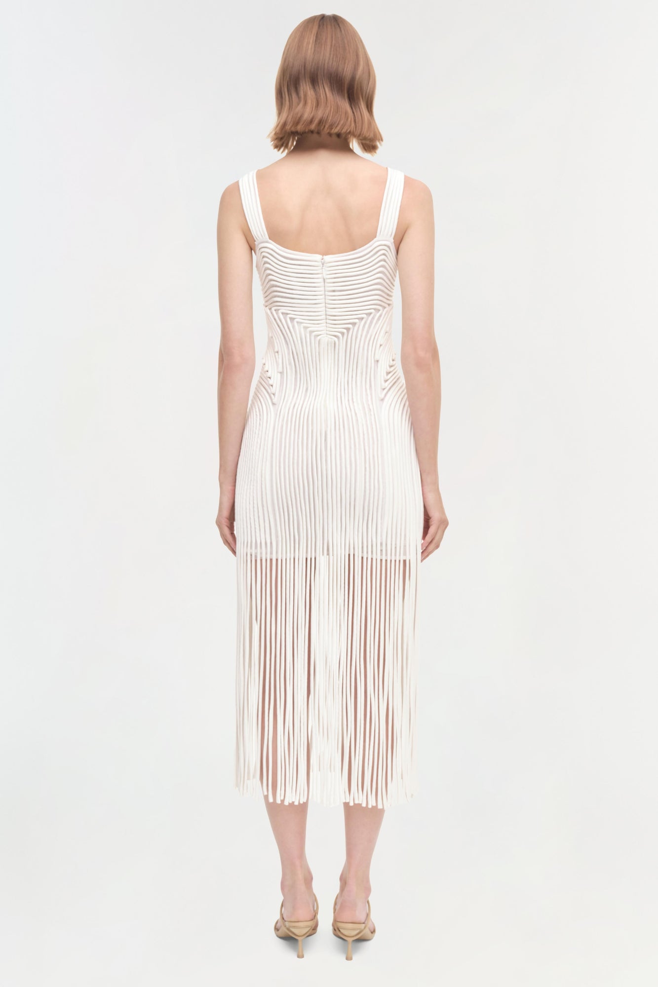 White sleeveless midi dress with vertical ribbed texture and fringe hem detail, shown from back view.