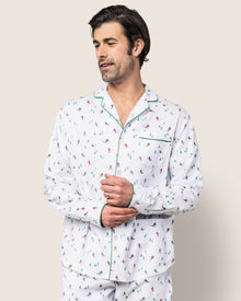 A man models the Mens Flannel Pajama Set in Apres Ski by Petite Plume. The classic white sleepwear showcases colorful skier prints and features green piping along the collar and pocket, adding a timeless touch to this luxury set against a plain background.