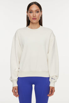 Model wears a white crewneck sweatshirt with logo on back that reads 