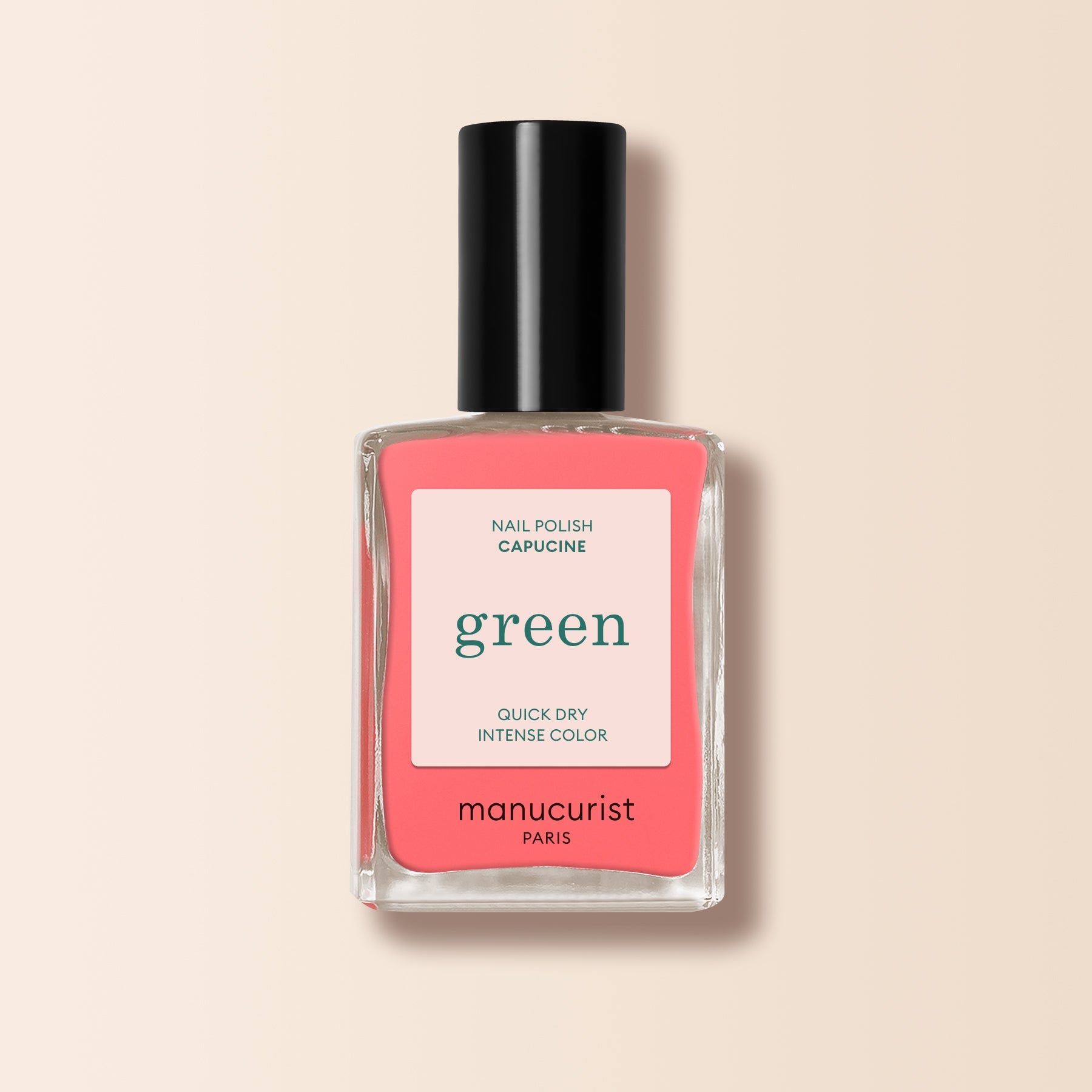 A bottle of Manucurist nail polish in the shade Capucine, coral pink from the Green range, with a black cap and "green, quick dry intense color" on the label, displayed against a soft beige background.