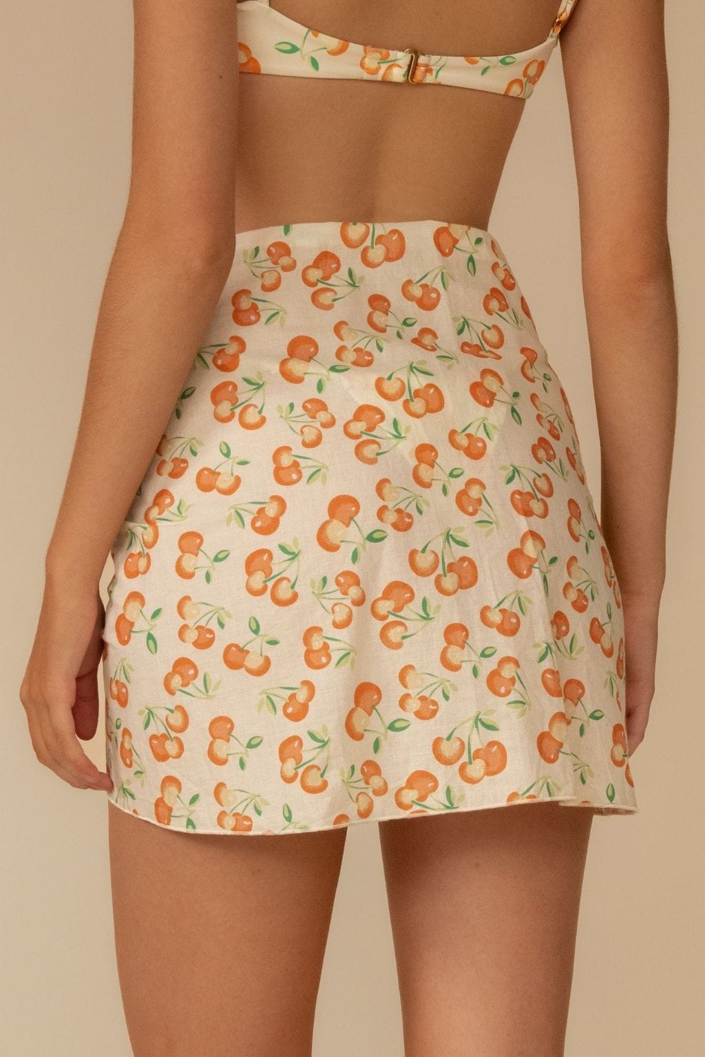 Cream sarong with all-over orange cherry and green leaf print, worn as a wrap skirt.