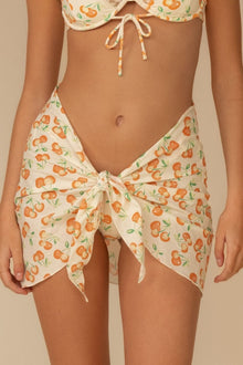 Cream-colored sarong with orange fruit and green leaf print, tied at sides with string closures.