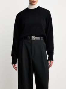 Model wearing Dehanche Louison black leather belt with white stitching and silver buckle, styled with black trousers and a black sweater