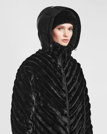 A person models the Rudsak ANASTASIA - 8124804 Black coat, featuring a textured, fur-like finish with diagonal stripes and a puffy hood, against a plain white background.