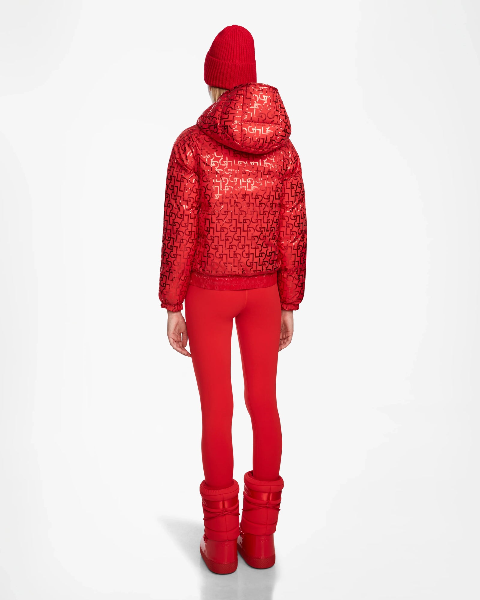 A person stands facing away, wearing the Rudsak DANI M - 8124539 Flame Red faux teddy ski jacket with a hood, paired with red leggings, a red knit beanie, and red boots against a plain white background.