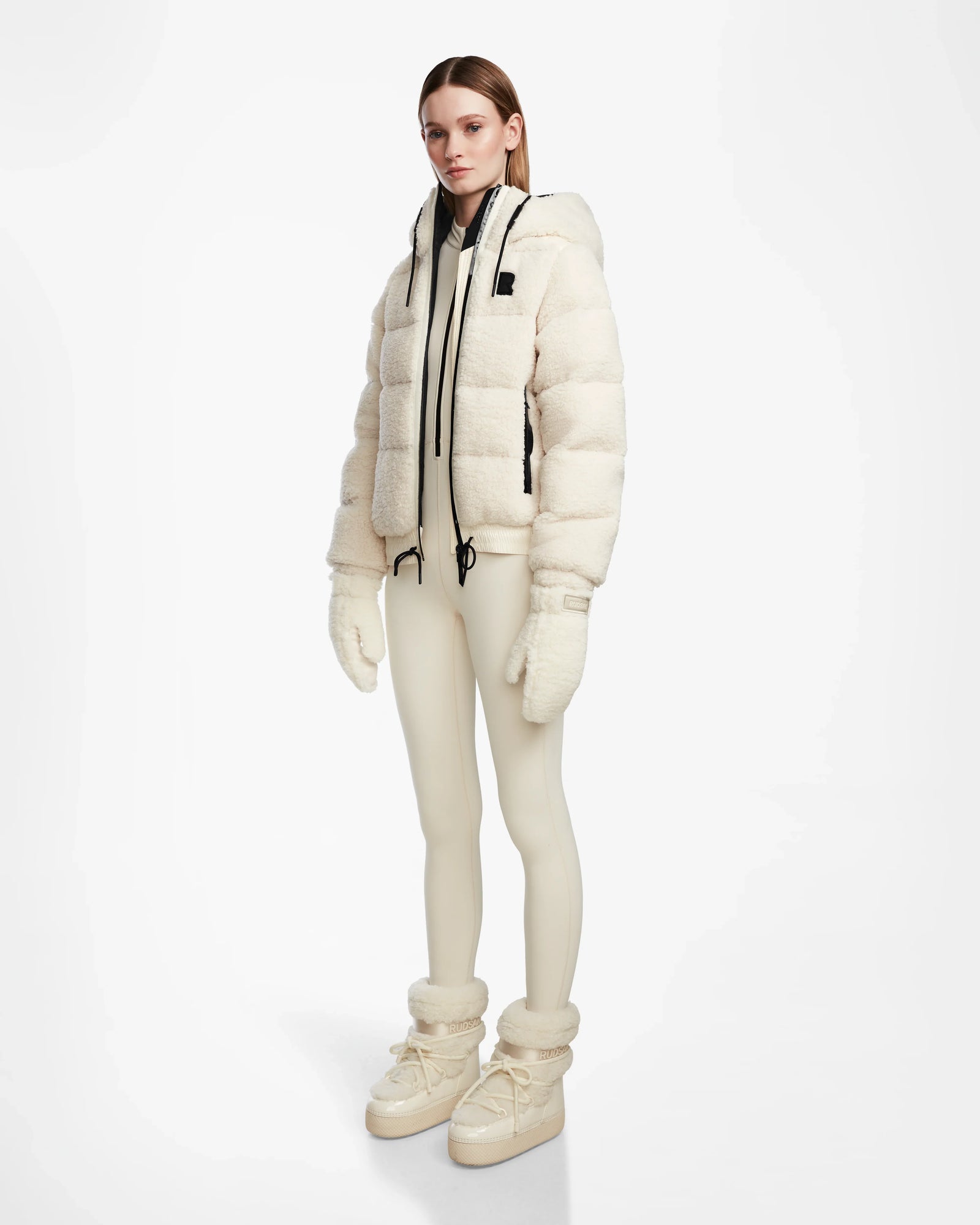 A woman stands against a white background wearing the Rudsak DANI S - 8124537 Iceland reversible cream ski jacket with hood, paired with matching leggings, mittens, and boots for a cozy, winter-ready look.