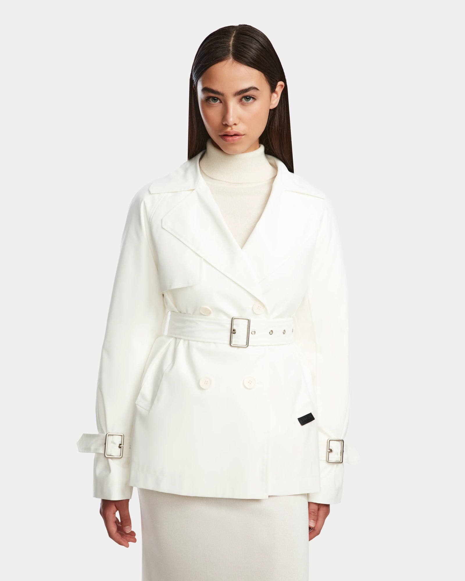 A woman stands facing forward against a plain light background, wearing the Rudsak ELENOR - 8124707 Iceland womens white trench coat with a shearling collar over a cream turtleneck sweater and skirt.