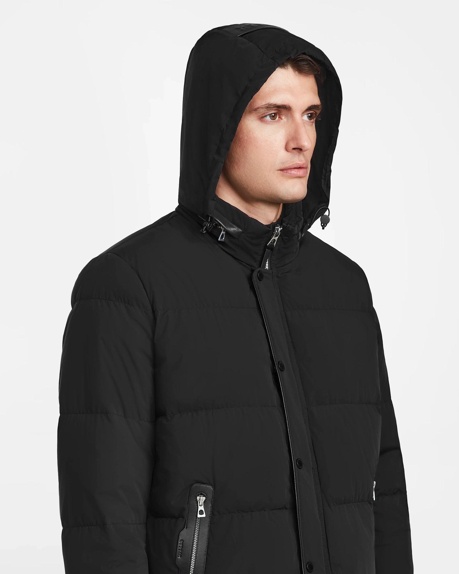 A man in a black Rudsak KARLS - M124505 mens puffer jacket with a hood looks to the right against a plain white background.