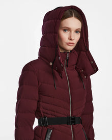 A woman wearing the Rudsak MALAYA M - L123554 Wine herringbone hooded jacket with a zipper and black belt, looking forward against a plain white background.
