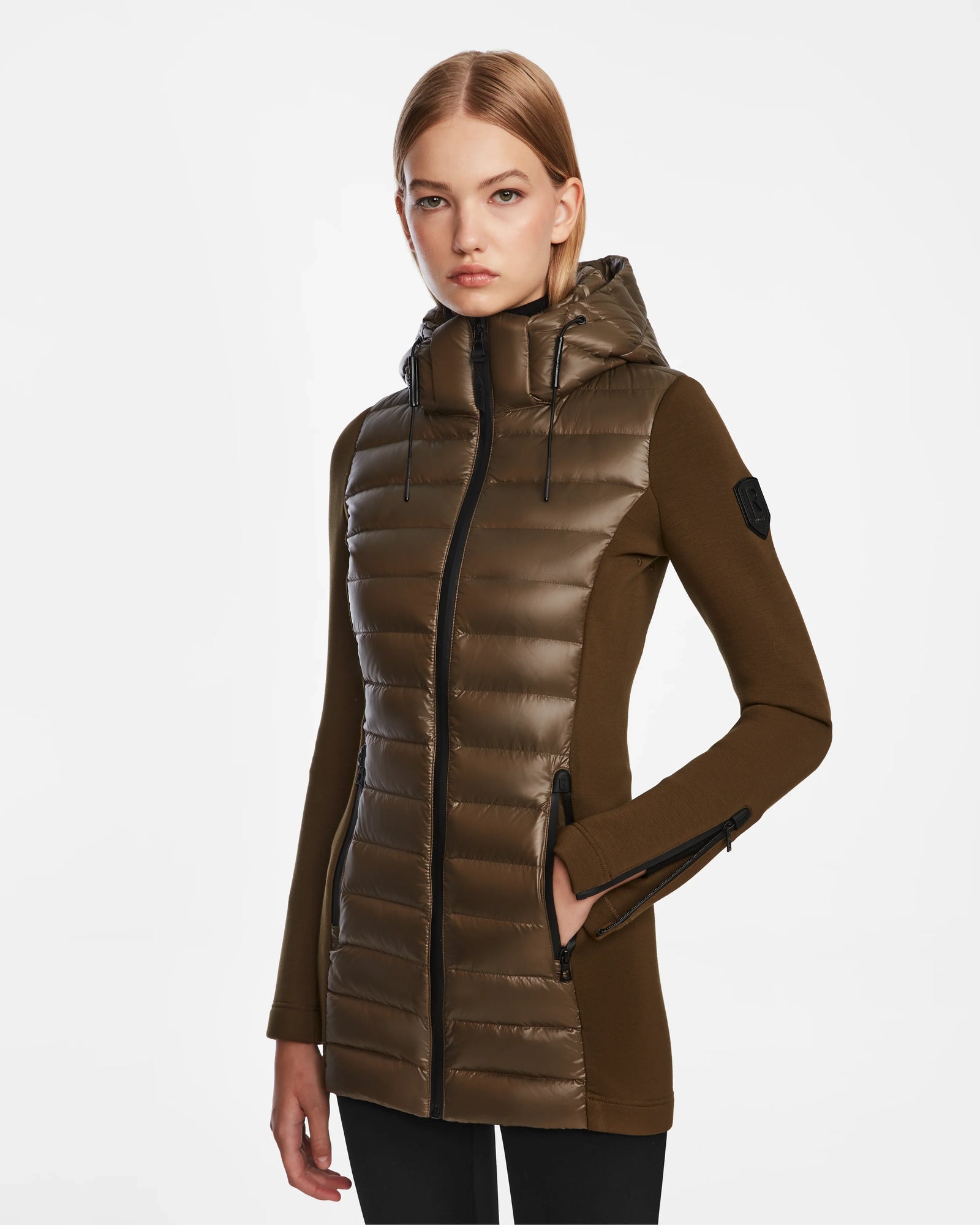 A woman with straight, shoulder-length blonde hair and a neutral expression wears the Rudsak MARRY - L121003 Light Olive women’s puffer jacket with waterproof zippers and black accents, standing against a plain white background.