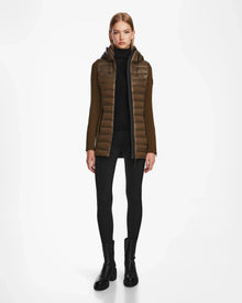 A woman faces forward, wearing the Rudsak MARRY - L121003 Light Olive womens puffer jacket with waterproof zippers over a black turtleneck, black leggings, and black ankle boots against a plain white background.