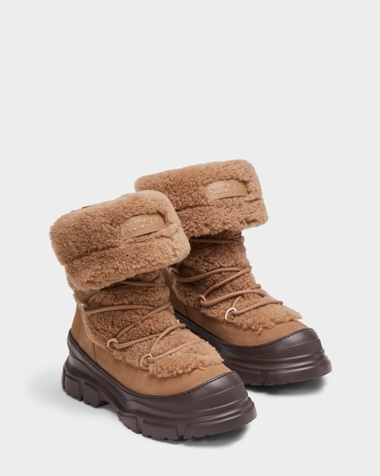 The Rudsak ROKI - 8224533 Camel are tan womens winter ankle boots with chunky dark brown soles, lace-up fronts, a soft faux shearling exterior, folded cuffs, and a stylish suede patch.