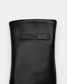 A close-up of the SELMA - 8424508 Black by Rudsak shows a black leather accessory with a rectangular Rudsak tag, set against a plain light gray background—a true winter essential.