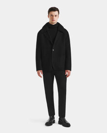 A man faces forward against a white background, wearing Rudsak’s AIDEN - 6125558 Black men’s wool-blend coat over a black turtleneck, paired with black pants and shoes for a refined outerwear look.