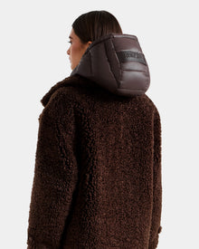 A woman wears the Rudsak EMRYN - L125588 Espresso women’s teddy jacket with a textured finish and shiny padded hood, shown from the back against a plain light background.