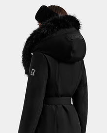 A person is shown from the back against a plain white background, wearing the Rudsak ISELLE - L125547 Black women’s belted down parka with a large furry hood and a matching black ear warmer.