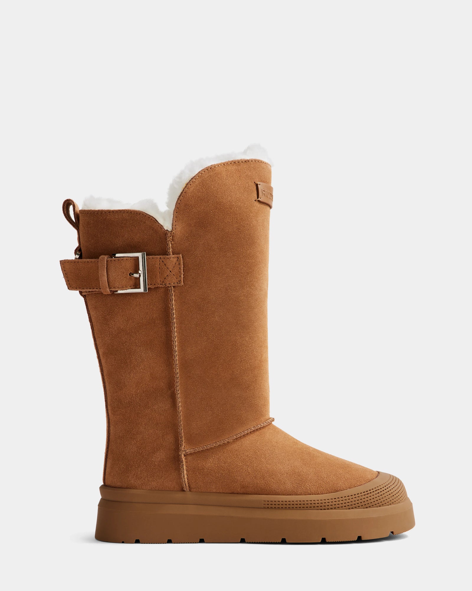 The Rudsak KLAIR - L225027 Tan is a women's mid boot in tan suede with a rubber sole, side buckle detail, and plush white wool lining peeking at the top, shown in profile against a white background.
