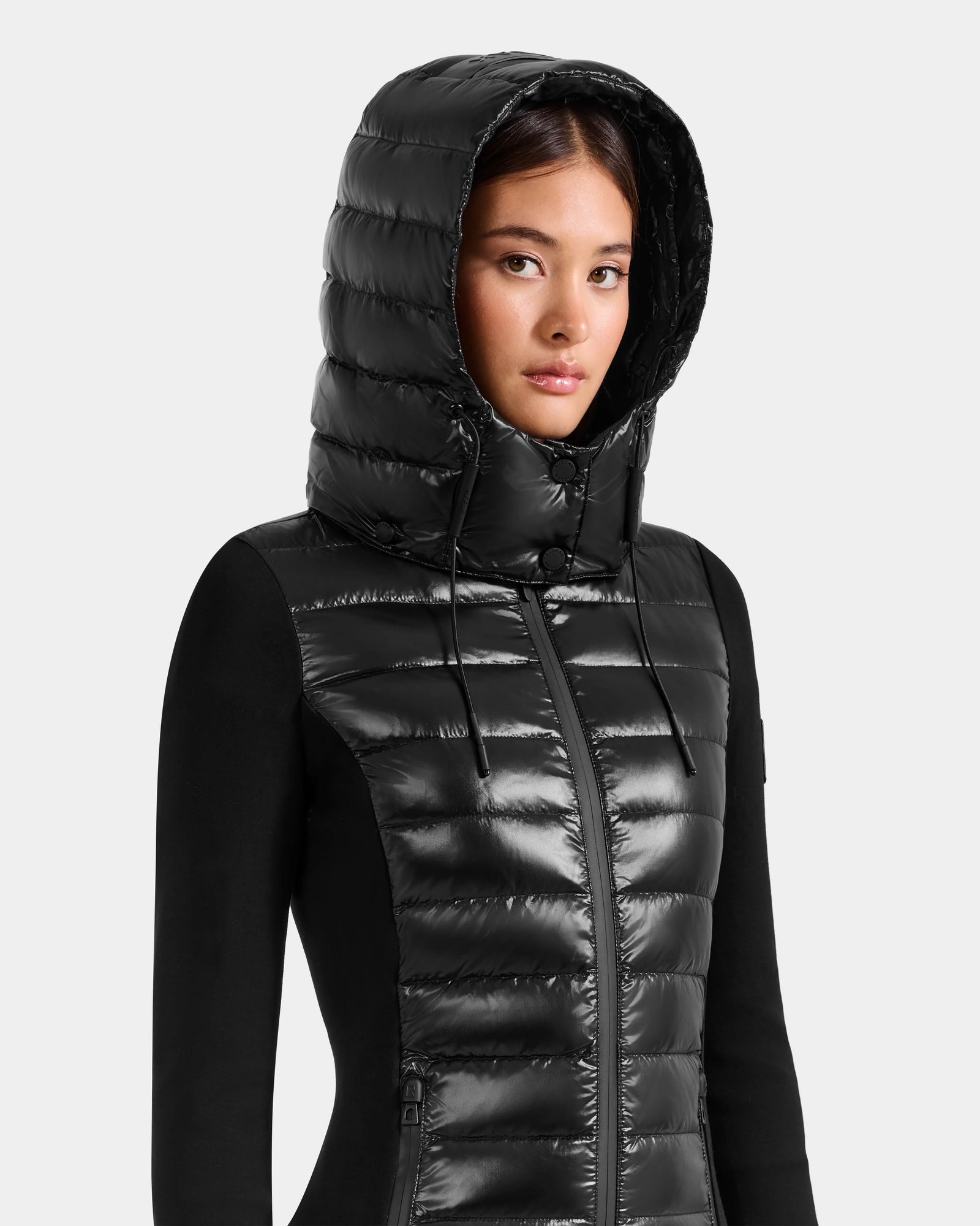 A woman wearing the Rudsak MARRY S - L125521 Black glossy shell jacket with a hood and front zipper, looking forward against a plain light background.