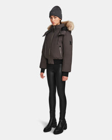 A person models the Rudsak MAUDE - L124522 Grey beanie, pairing it with a classic winter jacket with a fur-lined hood, black shiny leggings, and black boots against a plain white background.