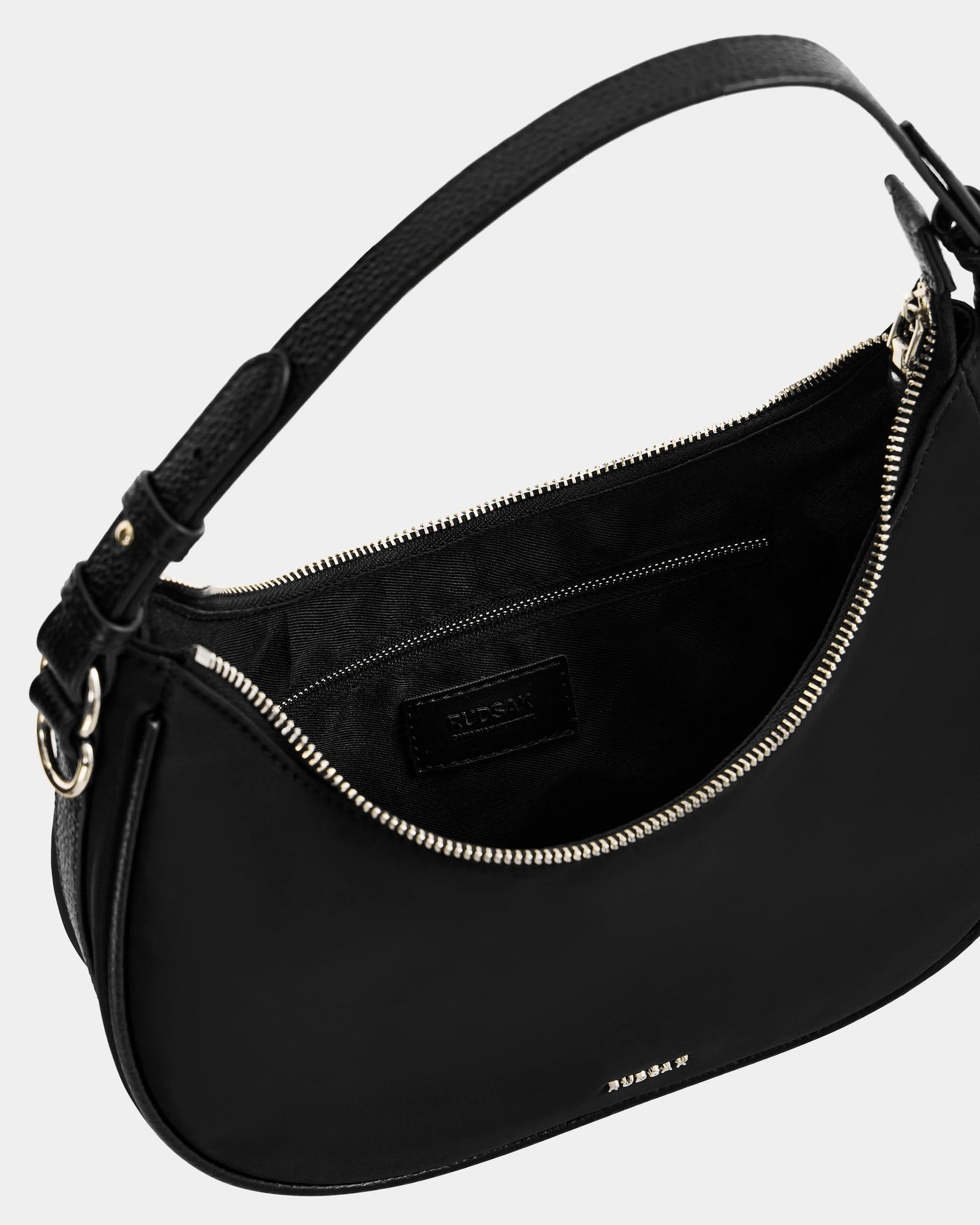 The Rudsak NIKKI - L325512 Black is a sleek women's black leather crescent shoulder bag with gold zipper, adjustable strap, inner pocket with stitched label, a hobo silhouette, and a fabric-lined interior.