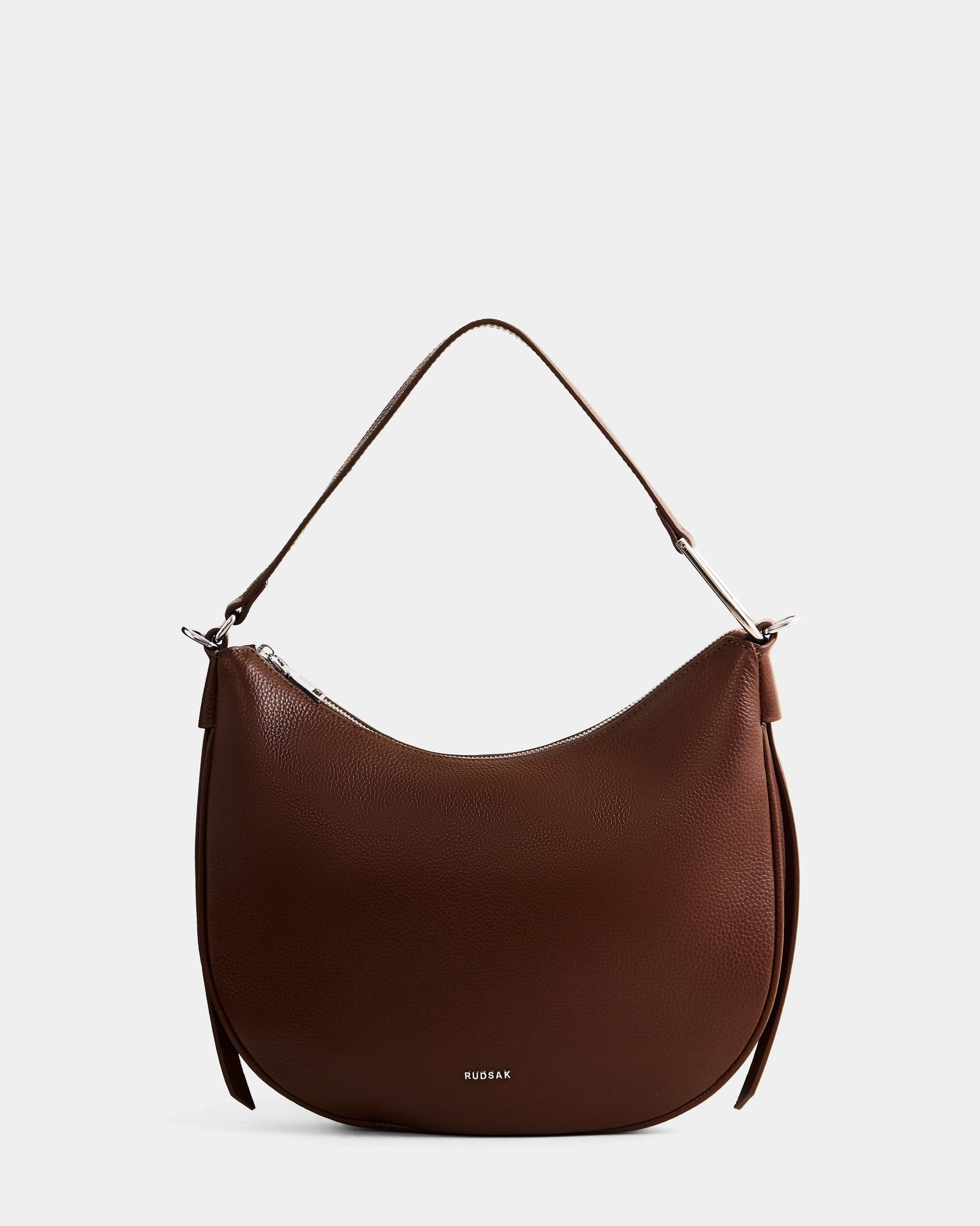 The SYLVIA - L325515 Mocha by Rudsak is a brown women's leather shoulder bag with a crescent silhouette, silver hardware, single strap, and subtle front branding, shown on a plain light background.