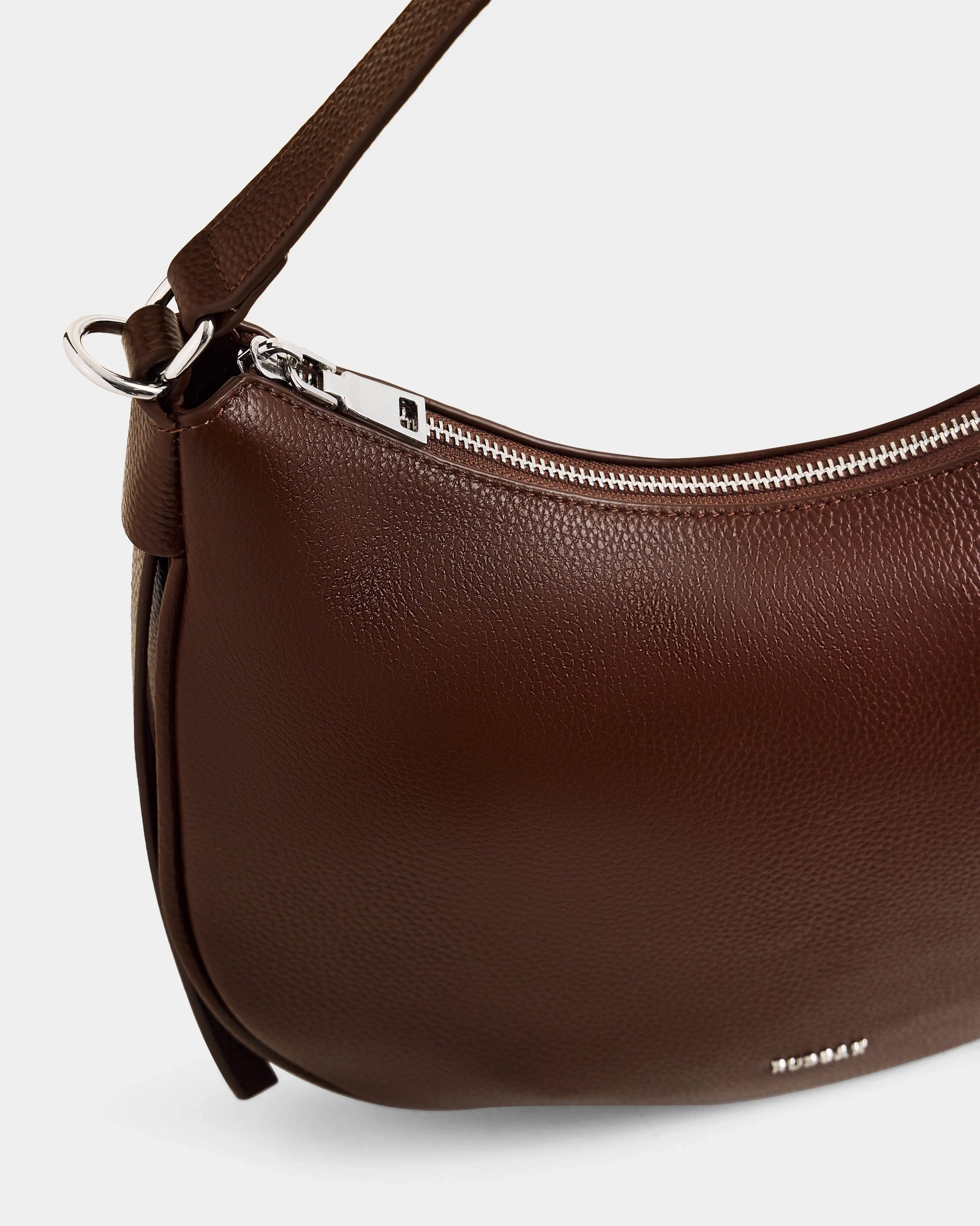 A close-up of the Rudsak SYLVIA - L325515 Mocha women's leather shoulder bag with a crescent silhouette, silver zipper, and short strap, shown against a plain light background.