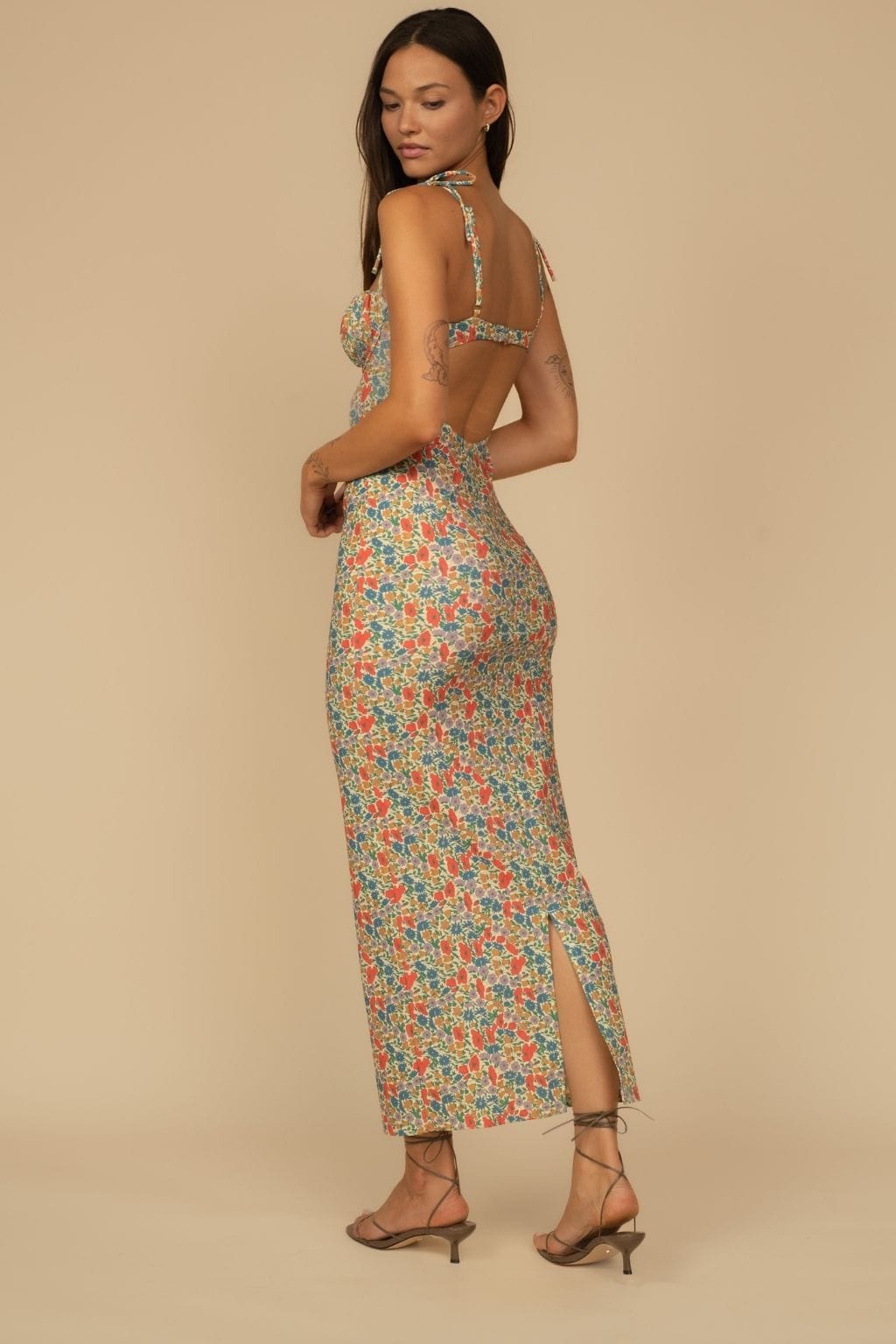 Woman wearing a colorful floral print slip dress with thin straps and an open back, paired with brown heeled sandals.
