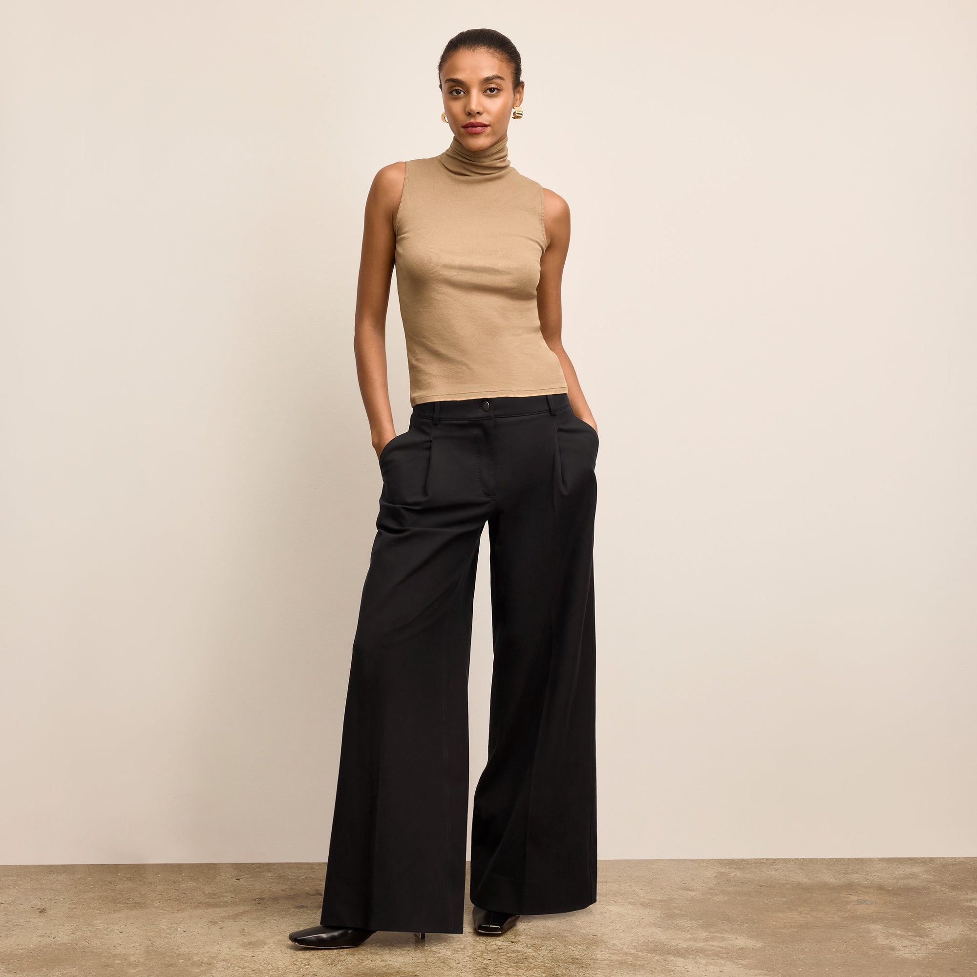 Woman wearing a beige sleeveless top and black wide-leg pants against a beige background
