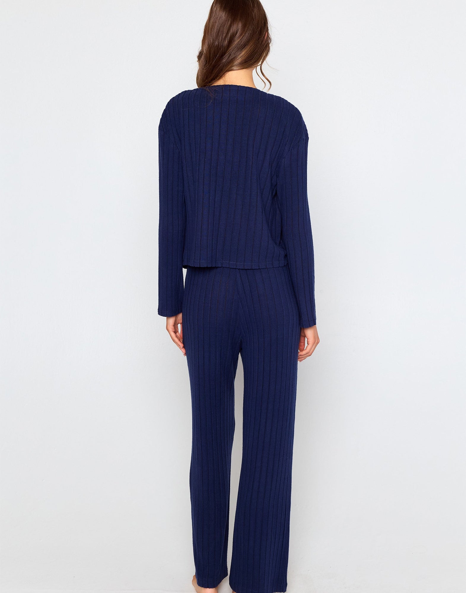 Woman wearing a navy blue ribbed long sleeve cardigan with front buttons, styled open over a matching bralette and pants.