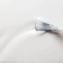 A close-up of a brush spreading smooth, white cream or lotion, creating gentle ripples on the creamy surface.