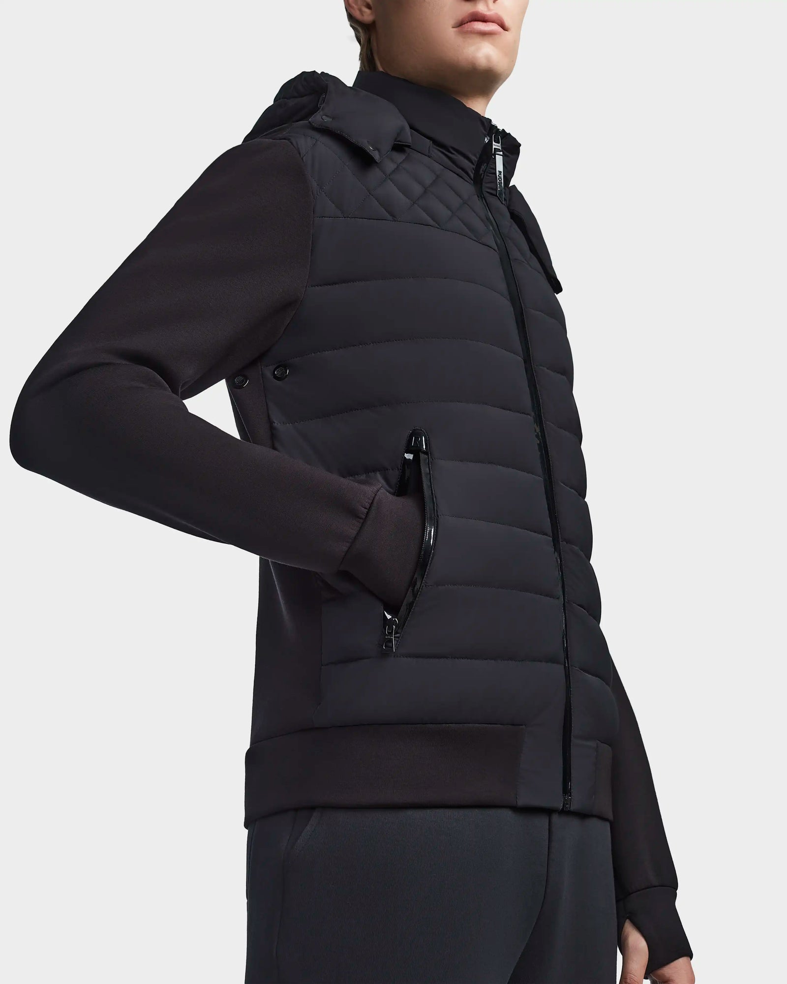 A person wears the Rudsak LAURENZO - M123514 Black quilted zip-up puffer vest with removable hood over a black long-sleeve top and dark pants, standing against a plain white background.