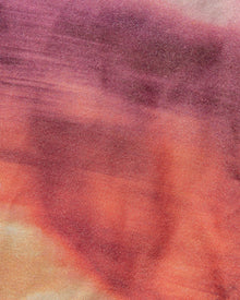 Close-up of a fabric with a tie-dye pattern in shades of purple, orange, and pink.