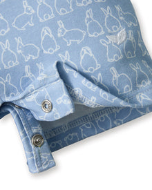 The Baby's Pima Louis Play Romper in Hoppy Days Blue is a light blue short-sleeve romper with a white collar and sleeve cuffs, a white bunny outline pattern, and bottom snaps for easy changing.