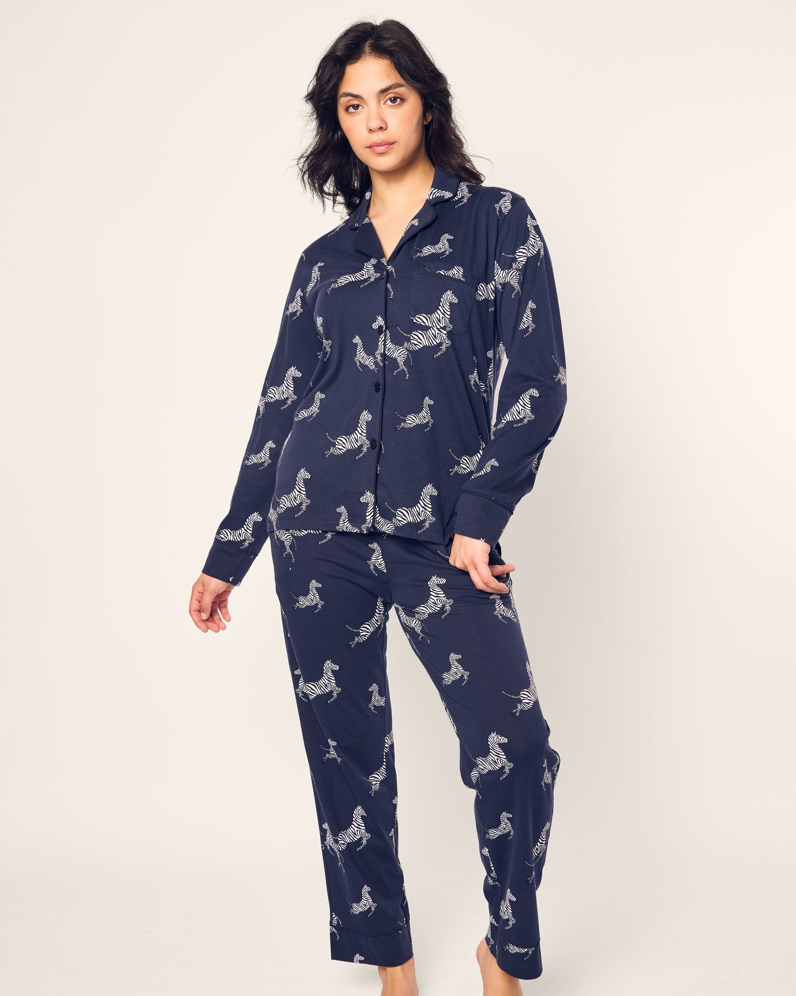 Against a plain backdrop, someone is dressed in the Petite Plume Womens Pima Pajama Set in Zebre de Nuit, featuring a luxury zebra print in navy and crafted from soft Peruvian Pima cotton.