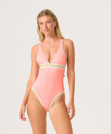 Woman wearing a pink one-piece swimsuit with gold trim on a white background