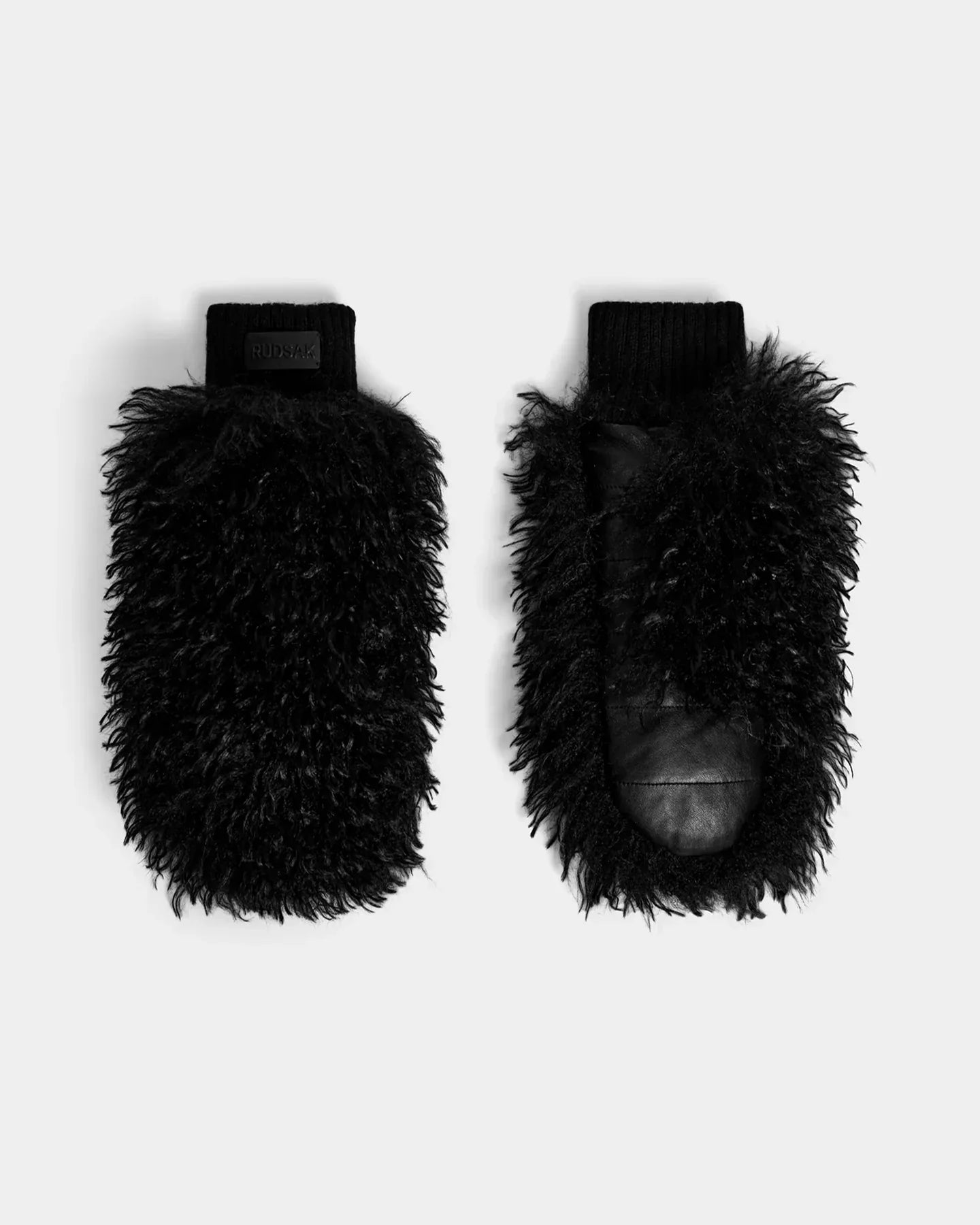 The SUSAN M - 8424505 Black by Rudsak are women’s faux Mongolian fur mittens with a fluffy, curly texture and ribbed knit cuffs, shown on a light gray background—ideal for après-ski style.
