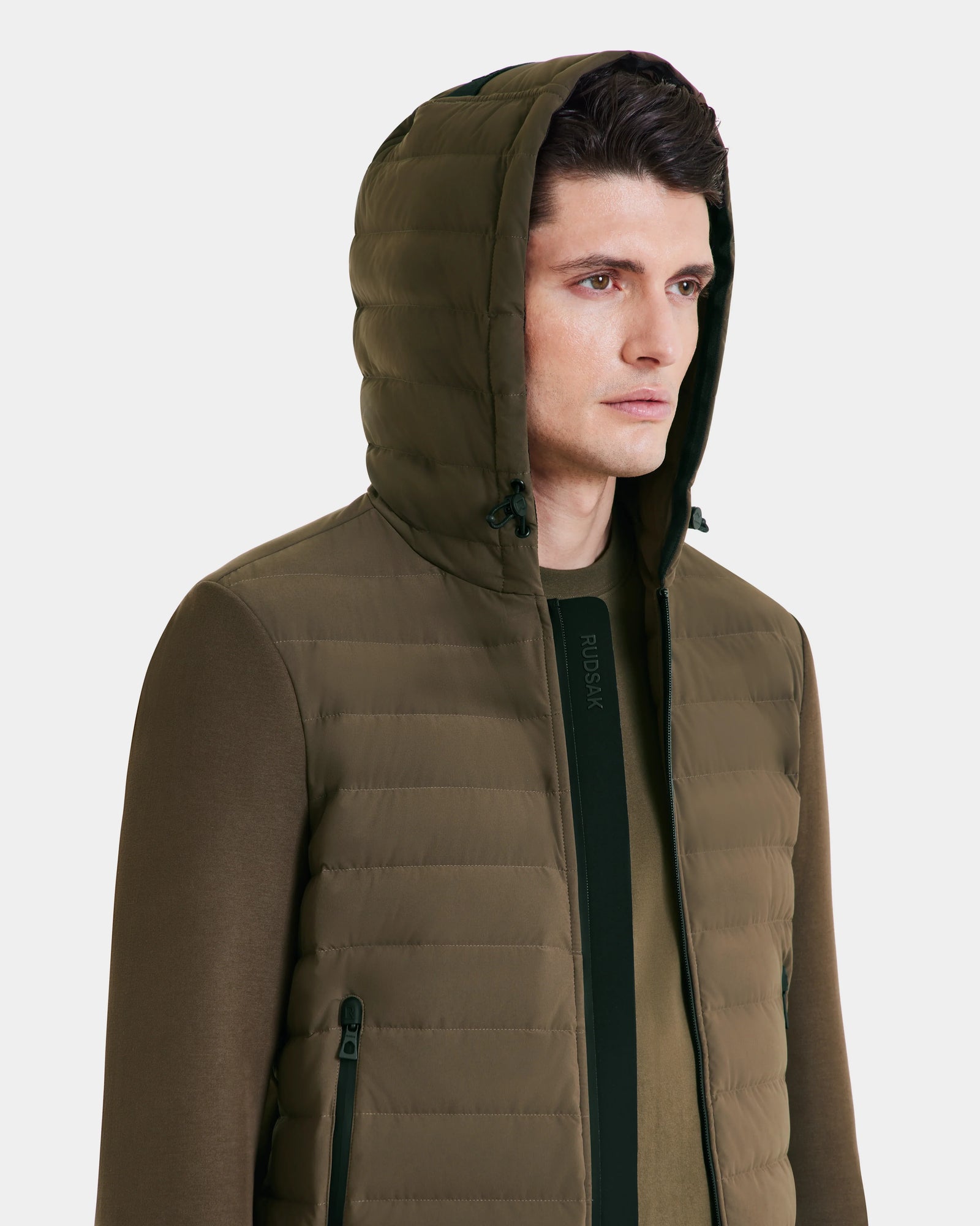 A person wearing the Rudsak DEE MAT - 6124028 Army mens olive green lightweight hybrid down jacket with zipper and side pockets, looking slightly to the side against a plain light background.