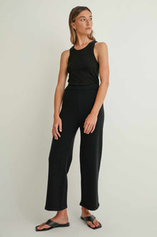 Woman wearing a black sleeveless top and pants on a light background