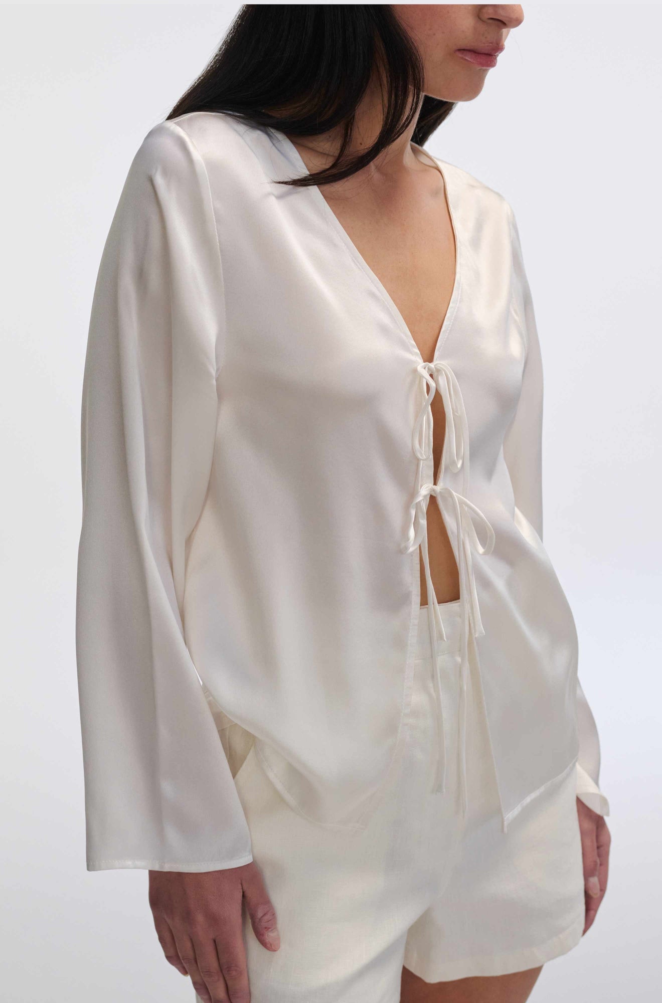 White satin outfit with long sleeves and shorts on a plain background