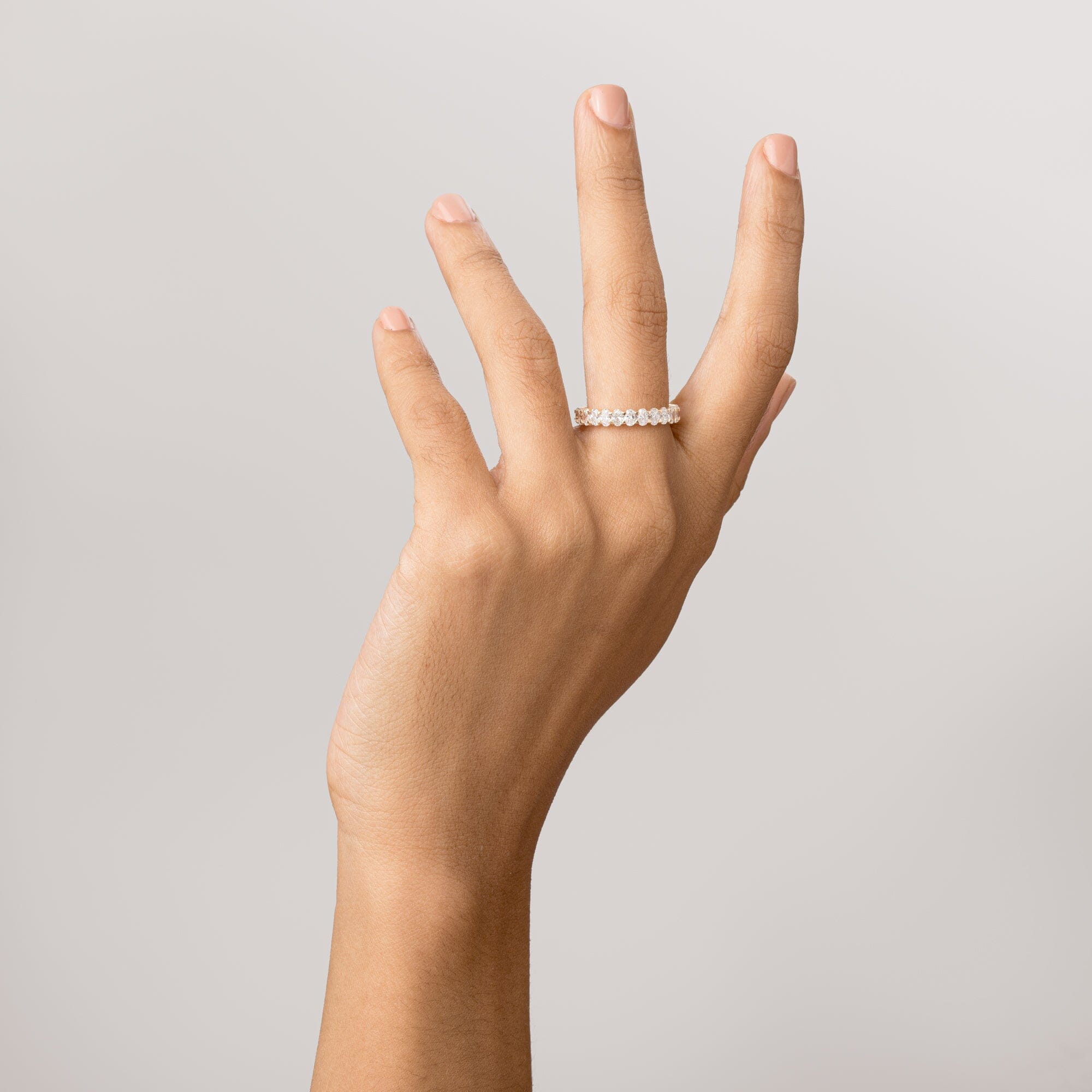 Model Close-up of a woman's hand with fingers gently curled upward, wearing a gold oval diamond eternity ring.