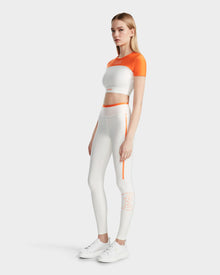 A woman wears the Rudsak LILIANE - 8524018 Eggshell women’s fitted crop top and high-waisted leggings, made from high-performance stretch fabric, paired with white sneakers against a plain light background.